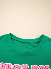 Green crewneck sweatshirt with pink embroidered holly jolly lettering, machine wash, slightly stretchy fabric care instructions