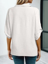 A soft off-white johnny collar roll-up sleeve blouse in white textured fabric with subtle texture and three-quarter sleeves