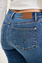 Back view of blue judy blue mid-rise stretch capri jeans with brown leather patch and stitched heart on back pocket