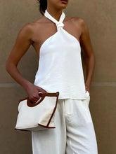 White canvas tote bag with brown leather handles and trim paired with a knotted halter neck cami product display