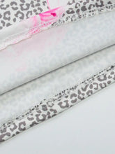 Stacked fabric pieces of a gray leopard cami with pink floral accents white stitching and lace detail ruched bodice