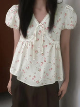 A delicate off-white short sleeve blouse with soft pink floral pattern and lace trim around the neckline
