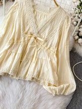 A cream-colored lace detail v-neck blouse with ruffled tiers and a matching ribbon tie at the waist