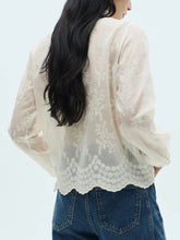 A delicate off-white lace sheer long sleeve blouse with floral embroidery and scalloped hem