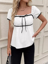 White blouse with black lace trim and matching ribbon tie at the neckline in short sleeve style