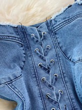 Back view of blue denim a-line mini dress with lace-up back, silver-toned eyelets, and frayed edges