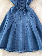 A medium-wash denim dress with a corset-style lace-up front and a pleated a-line mini skirt