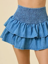 A denim skirt with a smocked waist and three layered ruffle tiers in blue denim fabric