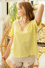 Woman modeling lemon yellow short sleeve t-shirt with criss-cross V-neckline and frayed white denim shorts
