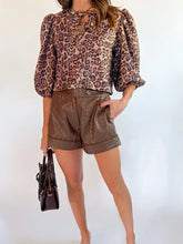 Brown quilted faux leather shorts with button closure and rolled cuffs paired with leopard bow tie puff sleeve blouse