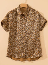 A short-sleeved leopard print button-down shirt with metallic gold and brown pattern on a wooden hanger
