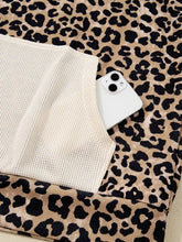 White smartphone with dual-camera system resting on leopard print fabric next to slightly stretchy machine wash leopard print hoodie