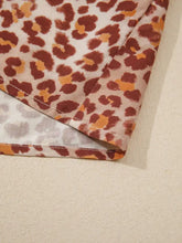 A cream-colored leopard print smocked notched blouse with bold rust and warm orange tones on soft fabric