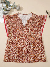 A women’s leopard print smocked short-sleeved blouse with red trim and a v-neckline in brown and tan shades