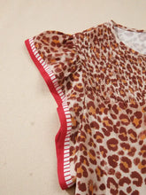 A women’s leopard print smocked notched blouse with brown and beige print, flutter sleeves, and red white trim