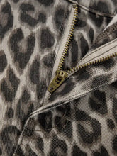 A close-up of a leopard-print denim jacket zipper with olive-green pull tab paired with leopard straight loose leg jeans