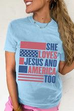 Light blue round neck short sleeve t-shirt with distressed American flag graphic and she loves Jesus and America too text in red, white, and blue