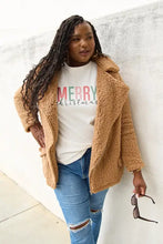 Woman in tan teddy fleece jacket with merry Christmas short sleeve shirt and distressed jeans