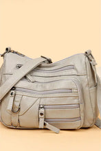 Light gray leather crossbody bag with zippered compartments and adjustable strap