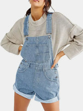 Light wash pocketed square neck wide strap denim overalls shorts with cuffed hems over beige sweater
