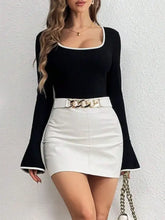 Black long sleeve bodysuit with white contrast trim and flared cuffs paired with white faux leather mini skirt and gold belt