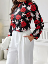 Long sleeve floral print blouse with red rose design, white pants, clutch