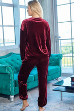 A woman wearing a burgundy velvet long sleeve top and pants lounge set with tapered pants and natural waistline