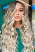 Woman in teal top wearing long wave heat safe blonde wig with ombre and highlights
