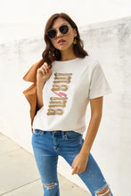 Woman in mama short sleeve white graphic t-shirt, blue jeans, brown jacket