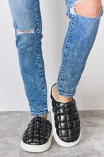 Person in ripped blue jeans wearing Melody Puffer Plush slippers with white soles