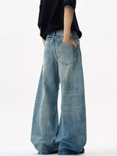Men’s distressed loose fit wide-leg denim jeans in faded blue wash with subtle distressing and raw hem detailing