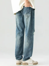Men’s blue denim relaxed fit jeans with faded wash and subtle distressing on the right leg