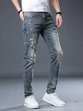 Men’s distressed slim fit blue denim jeans with colorful paint splatter accents and ripped detailing