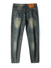 Men’s distressed slim fit dark-wash denim jeans with faded detailing and brown leather brand patch at the waistband back view