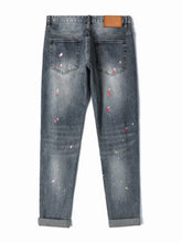 Men’s distressed slim fit dark-wash denim jeans with pink and white paint splatter and a brown leather patch