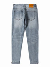 Light-wash men’s distressed slim fit jeans with rolled cuffs and an orange brand label at the waistband