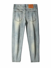 Back view of men’s distressed slim fit jeans in light-wash denim with faded details and brown leather patch
