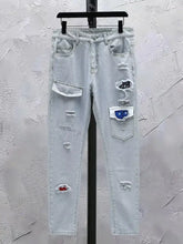 Men’s distressed wash jeans in light-wash denim with ripped details and decorative patches on the thighs
