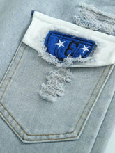 Men’s distressed wash jeans with a light blue denim pocket featuring a white frayed edge and royal blue embroidered patch