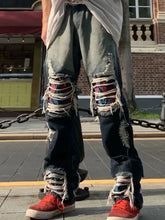 Men’s distressed wash loose fit denim jeans with heavily ripped knees, frayed edges, and colorful embroidered patches