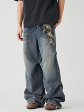 Back side of men’s distressed wide leg denim jeans in faded blue wash with plaid fabric detail at the back pocket