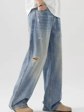Men’s distressed wide leg light-wash denim jeans with intentional distressing and ripped knee detail