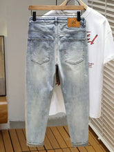 Men’s distressed wide leg jeans in light-wash denim with a slim fit and rolled cuffs hanging on a wooden hanger