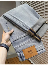 Men’s distressed wide leg light-wash denim jeans with brown leather patch and striped cuffs, back side view