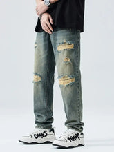Men’s distressed wide leg relaxed fit jeans in faded blue denim with multiple ripped patches and frayed raw edges