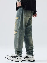 Men’s distressed wide leg relaxed fit jeans in faded green wash with multiple ripped patches along the legs
