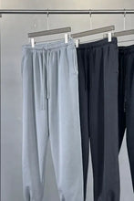 Three pairs of mens drawstring joggers in grey and black on rack