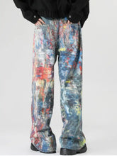 Men’s full size wide-leg denim jeans featuring vibrant abstract art print paint-splatter design in blue red and yellow