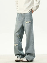 Men’s full size loose fit jeans in light distressed wash denim with frayed patches on thighs and knees