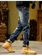Men’s slim fit distressed wash blue denim jeans with colorful embroidery paired with tan Timberland boots
